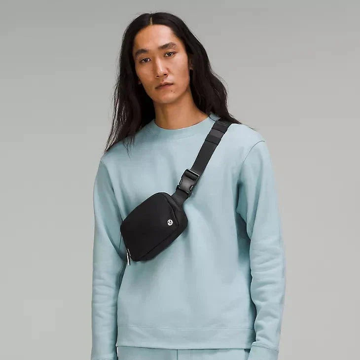 A man modeling the Lululemon Everywhere Belt Bag 1L in Black, worn over the shoulder, highlighting its adjustable strap and versatile wear for everyday use.