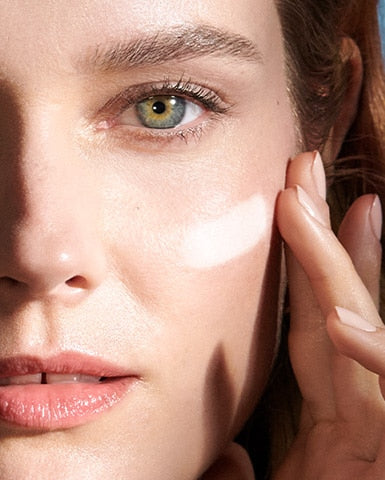 A female model applying Crème de La Mer, Moisturizing Cream to her face. The luxurious white cream visibly enhances skin texture and hydration, part of an effective anti-aging skincare routine.