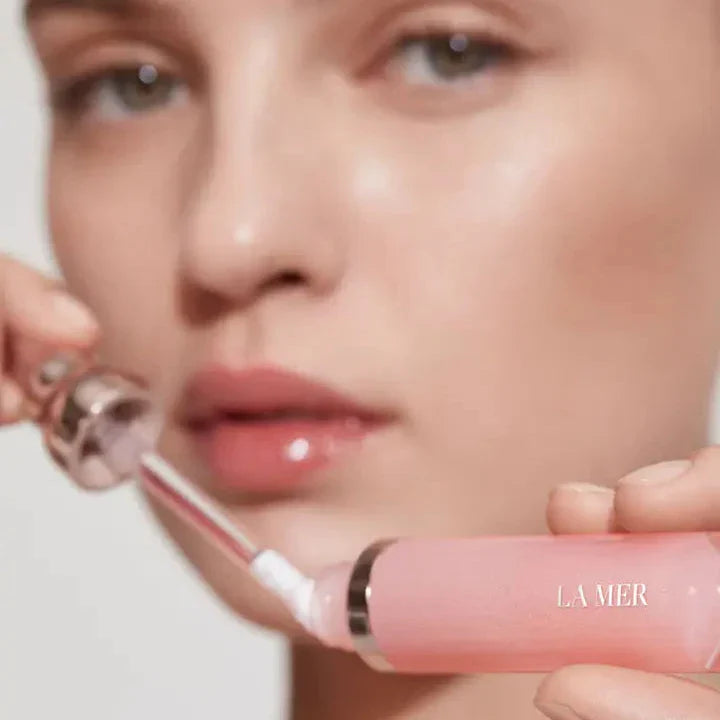 Close-up of a female holding La Mer The Lip Volumizer in one hand and its applicator in the other. She gazes at the camera, demonstrating the product's use for luxurious lip care.